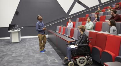 Man lecturing students in a university lecture theatre - one student is in a wheelchair