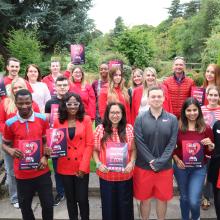 A group of CSP members pose outside, wearing red and holding red posters